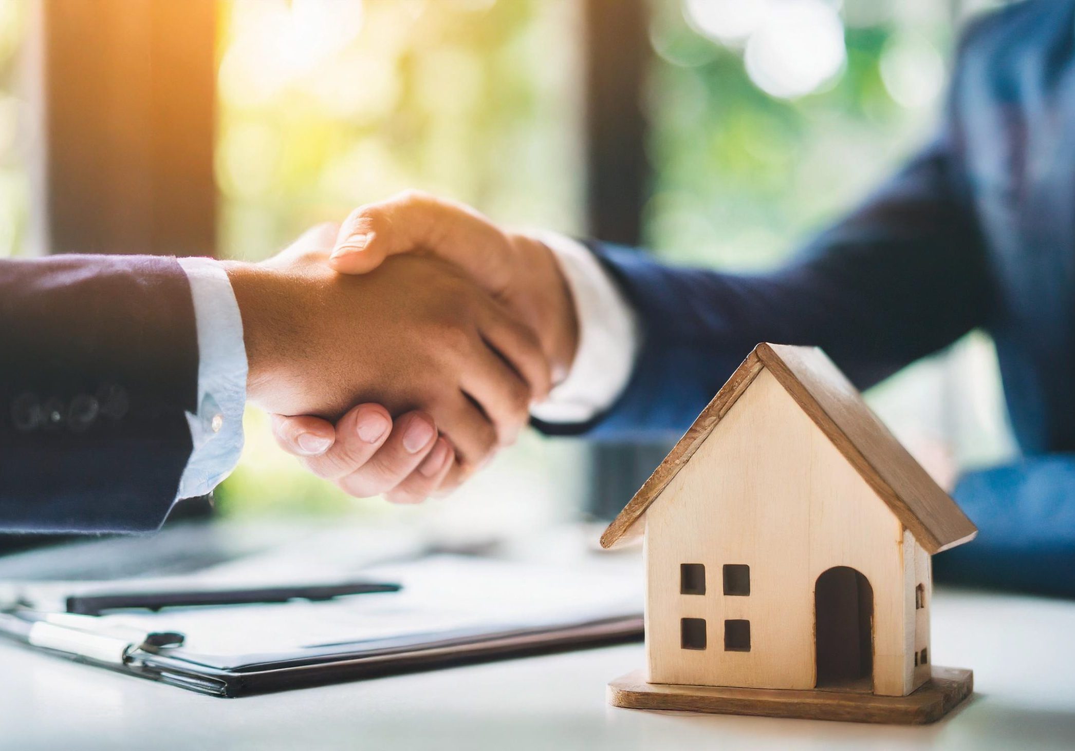 Business deal handshake over blurred wooden house on table, symbolizing agreement, partnership, real estate, success